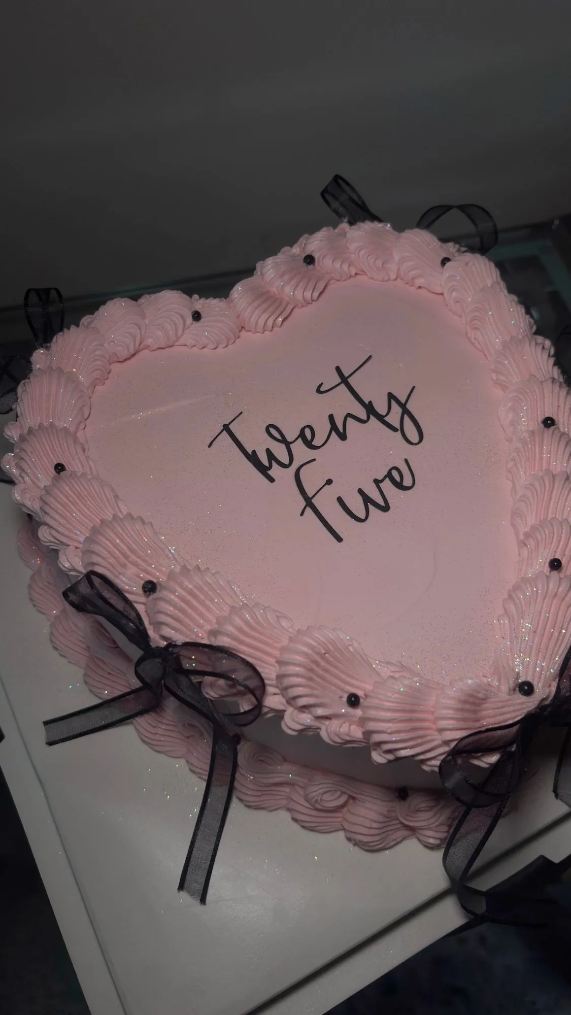 Pink heart-shaped buttercream cake with black ribbon bows and "Twenty Five" written in script